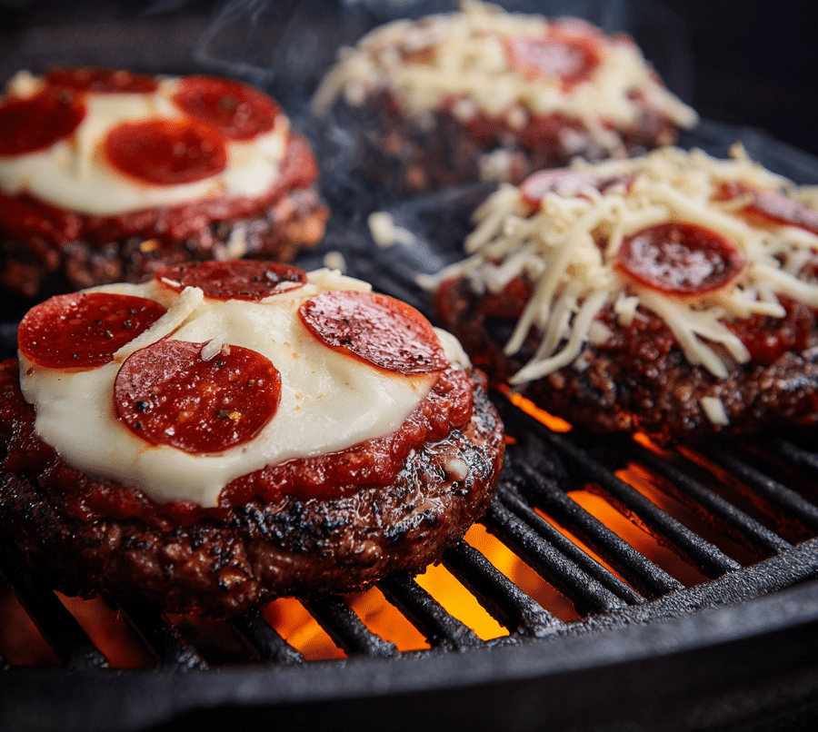 Pizza sauce, cheese, and pepperoni melting over burger patties on grill